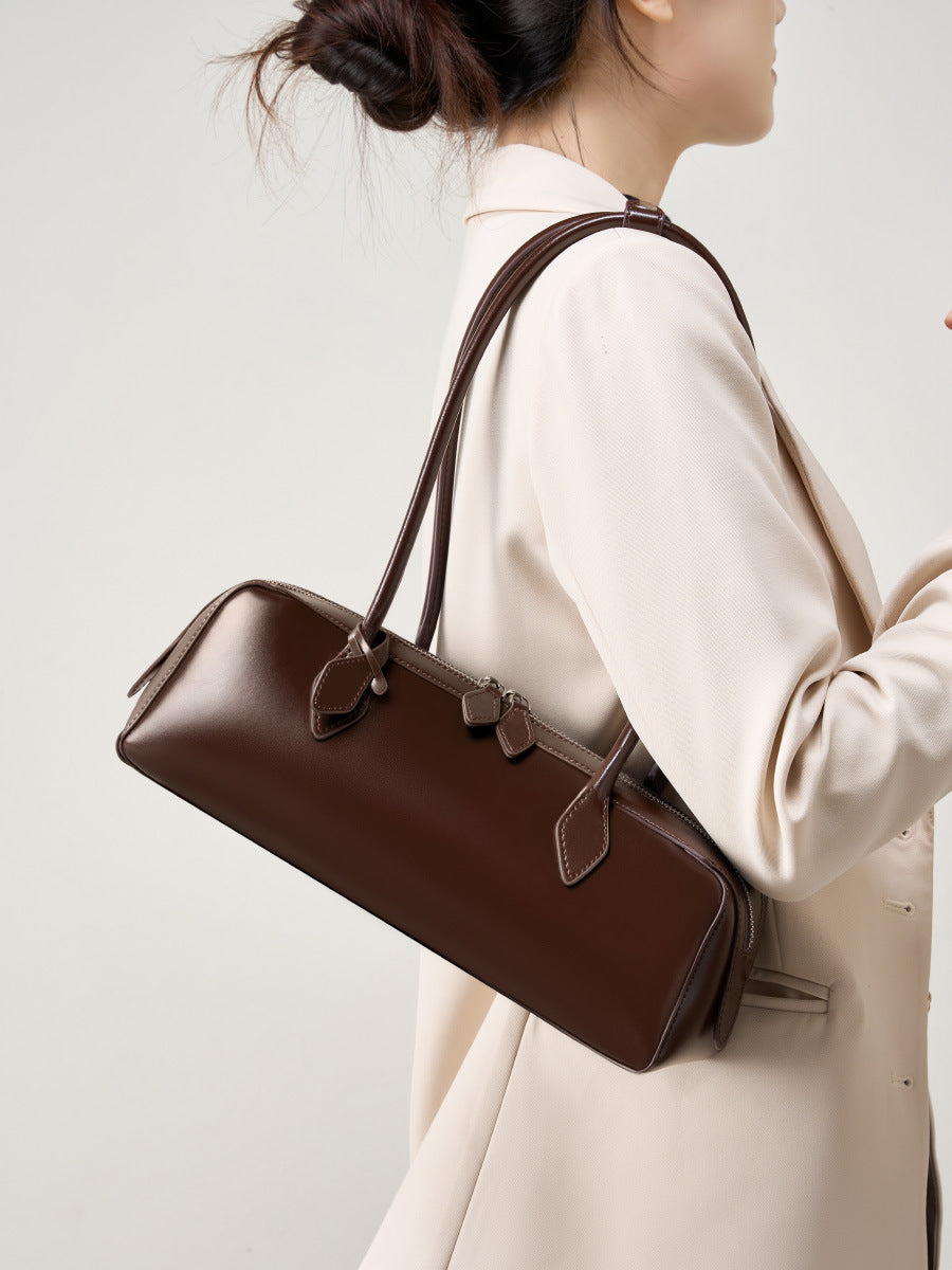 Elegant woman holding a winter leather baguette bag in brown, showcasing its stylish design and craftsmanship.