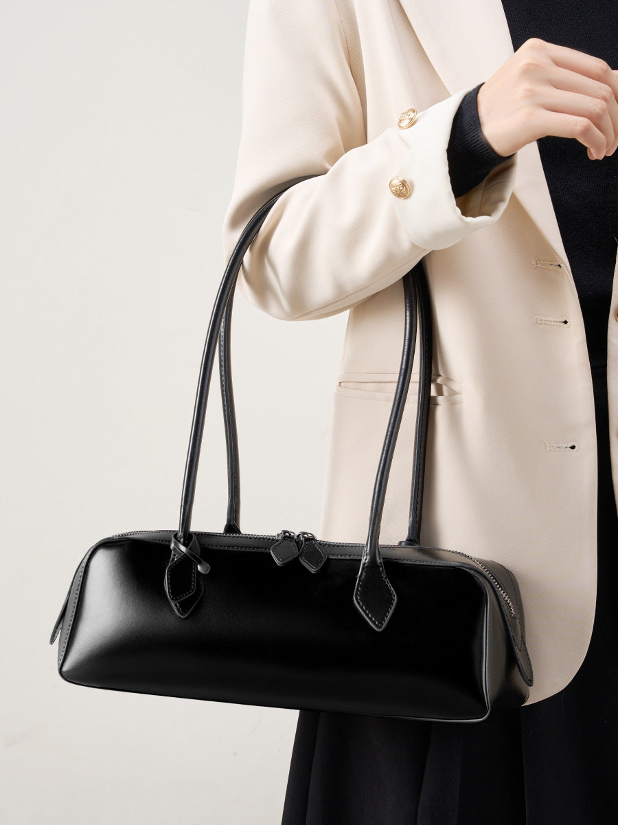 Woman holding a winter leather baguette bag in black, showcasing its elegant design and sleek structure.