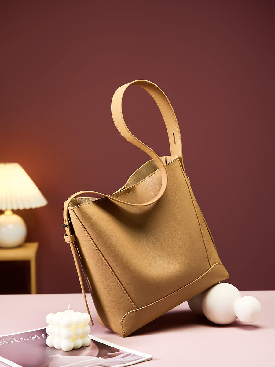 2026 genuine leather bucket bag in tan color with adjustable strap on a stylish table