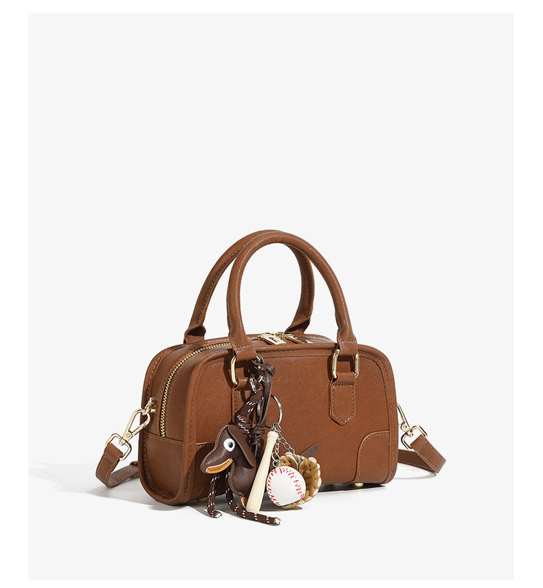 classic leather Boston bag featuring a glossy patina and playful keychain, ideal for stylish travel.