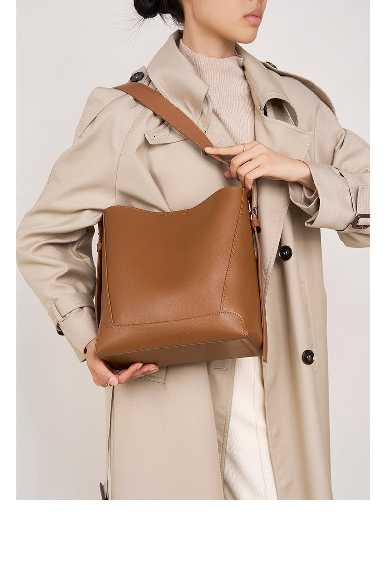Stylish woman holding a genuine leather bucket bag while wearing a beige trench coat.