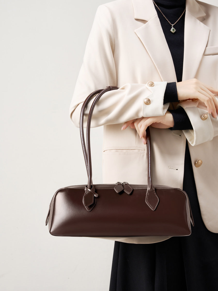Elegant woman holding a stylish brown winter leather baguette bag with structured design for versatile use.